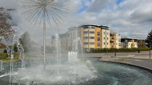 A fountain with water jets in a public square, surrounded by buildings and a clear sky. - The Pavilion by Select SA (Windsor)