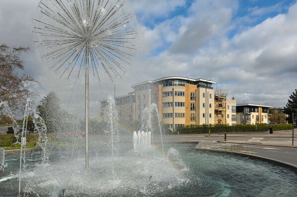 A fountain with water jets in a public square, surrounded by buildings and a clear sky. - The Pavilion by Select SA (Windsor)