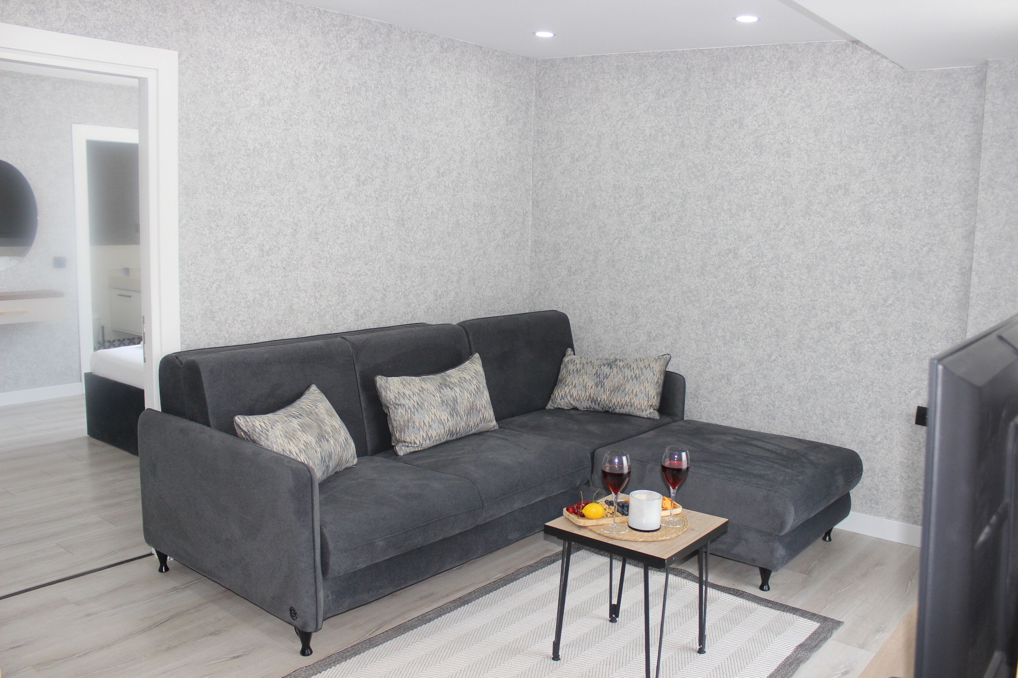Una sala de estar moderna con un sofá seccional gris, una pequeña mesa de centro de madera y un televisor de pantalla plana.