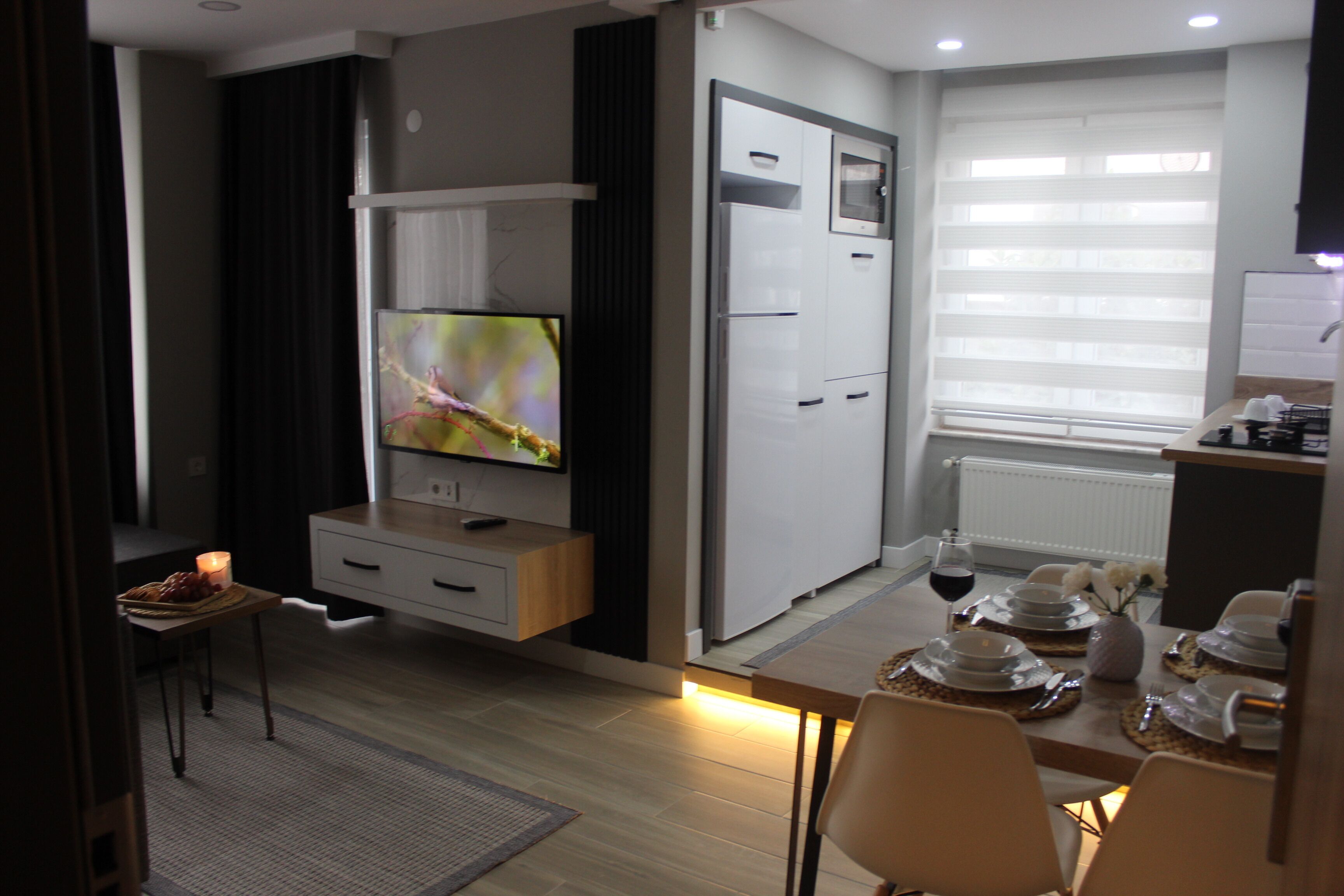 Eine moderne Küche mit Einbaukühlschrank, einem Essbereich mit Tisch für vier Personen und einem an der Wand montierten Fernseher.