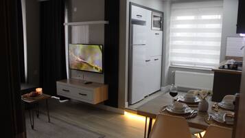 Eine moderne Küche mit Einbaukühlschrank, einem Essbereich mit Tisch für vier Personen und einem an der Wand montierten Fernseher.