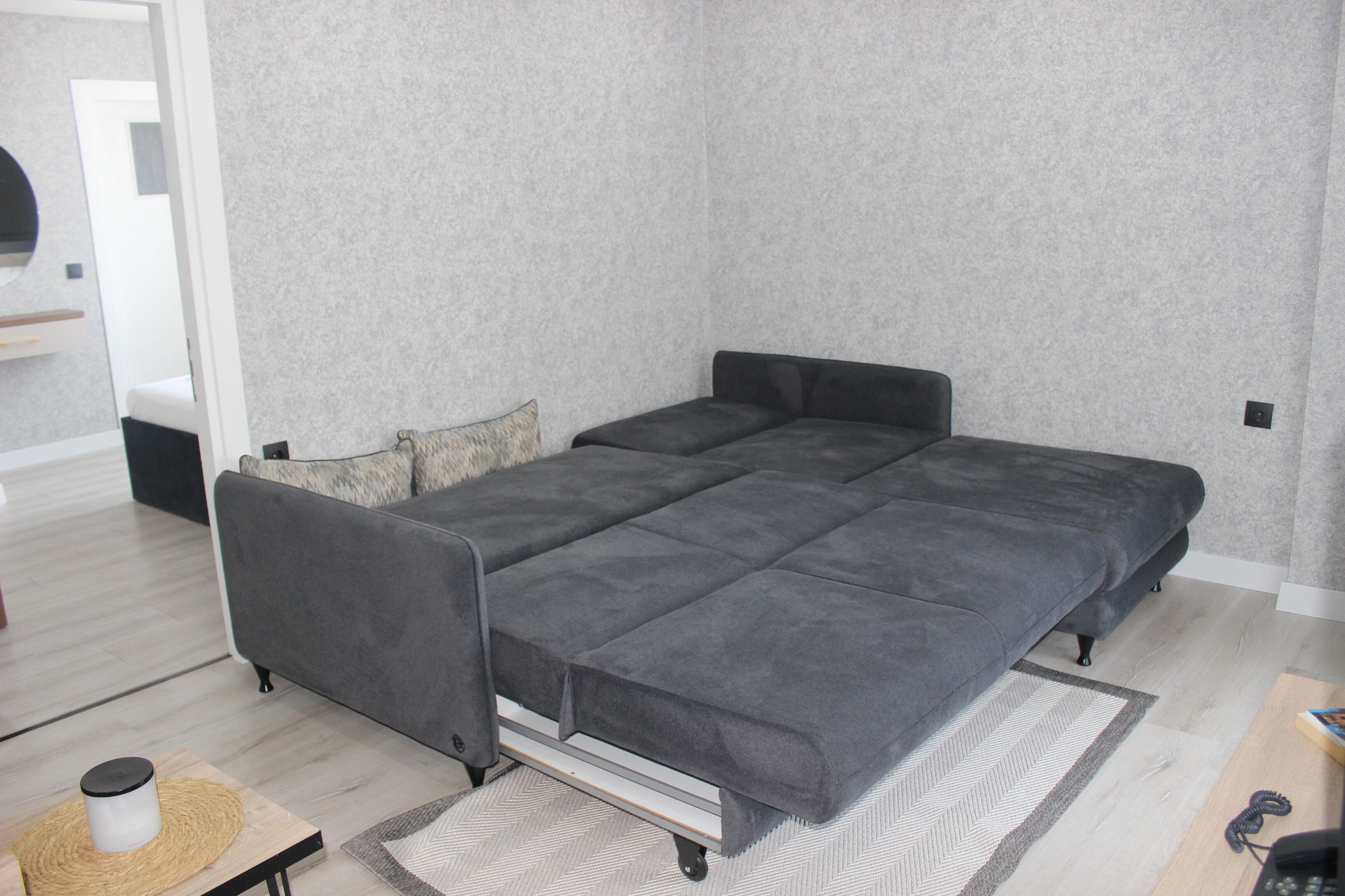 Een moderne slaapkamer met een grijze slaapbank, een klein nachtkastje en een kamerbreed tapijt met dessin.