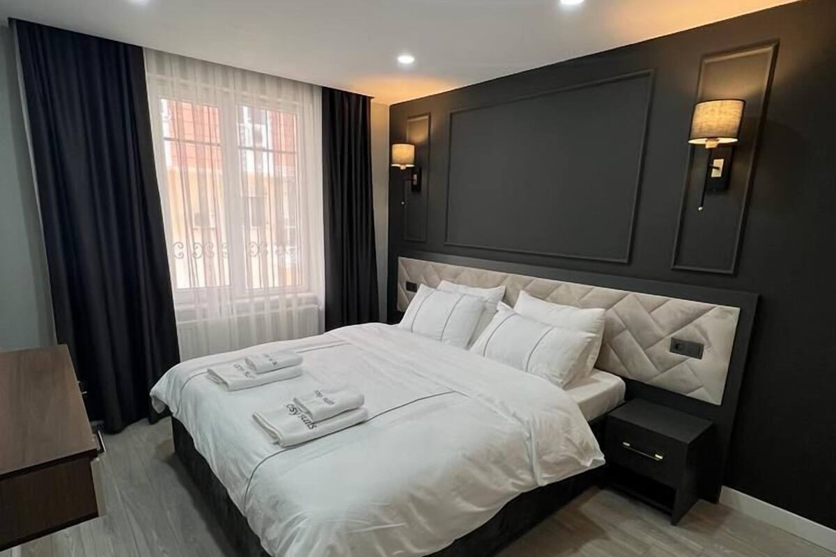 A modern hotel room with a large bed, dark walls, and a wooden floor.