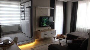 A modern living room with a flat-screen TV, a sofa, a dining table with a candle, and a kitchen area with a microwave and oven. - Cosy Suite Hotel (Konyaalti)
