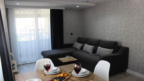 A modern living room with a grey sofa, a dining table set with plates, glasses, and a fruit platter. - Cosy Suite Hotel (Konyaalti)