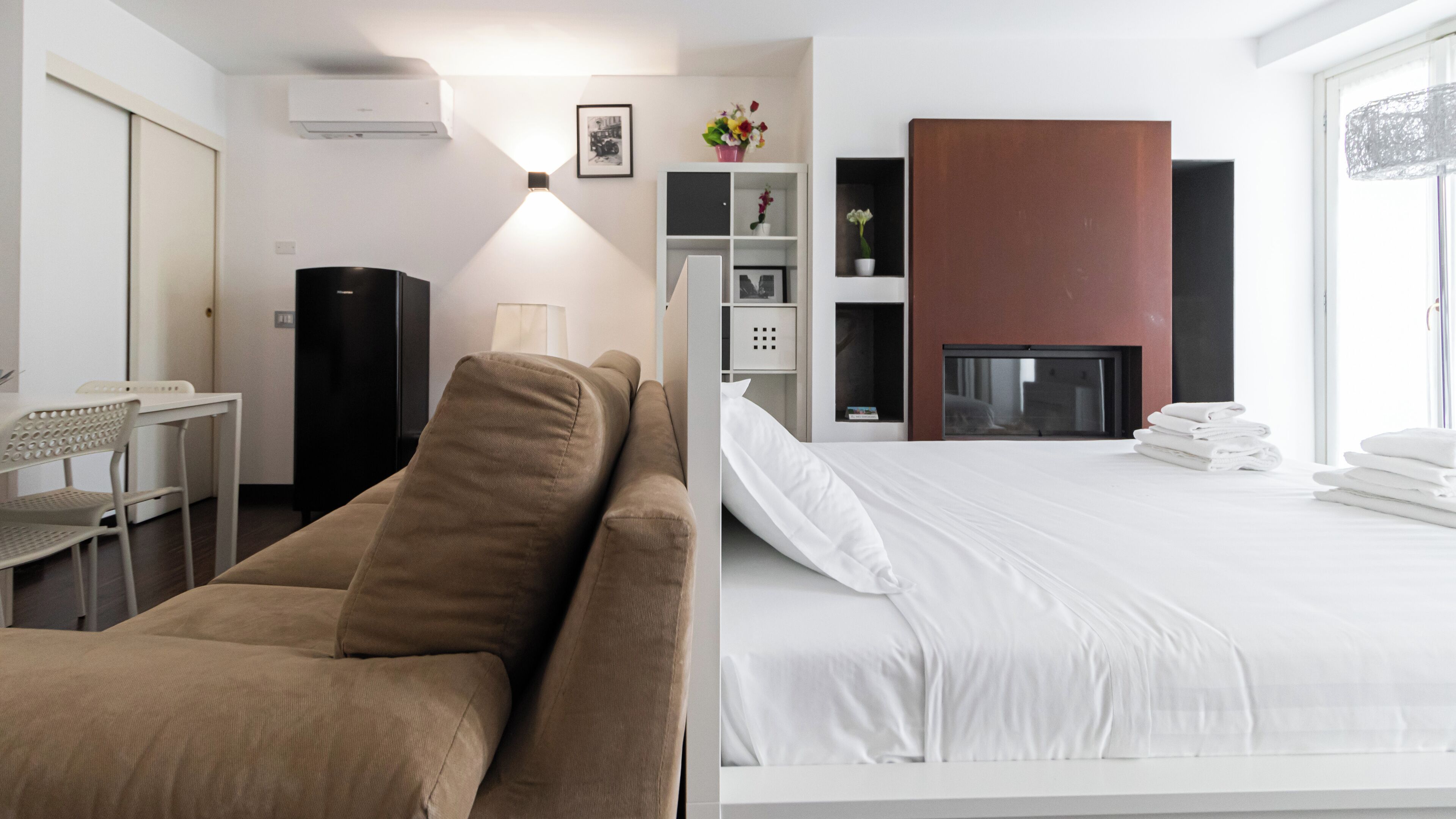 A hotel room with a bed, a sofa, a desk, a TV, and a fireplace.