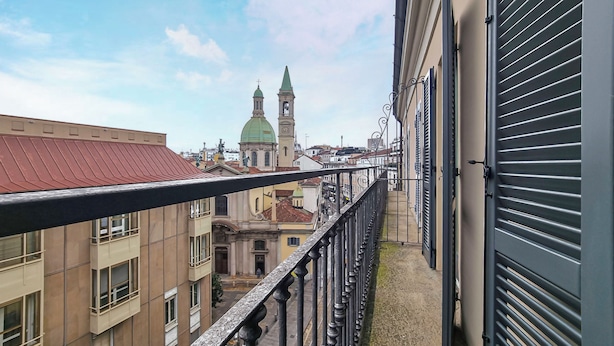 Un balcón con vista a una iglesia de dos torres y un reloj, rodeada de edificios con balcones y un tejado rojo.