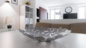 Un salón moderno con una mesa blanca, un sofá marrón, un armario blanco y un reloj montado en la pared.
