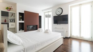 Una habitación de hotel moderna con una cama grande, un televisor de pantalla plana, un reloj y una ventana con vistas.