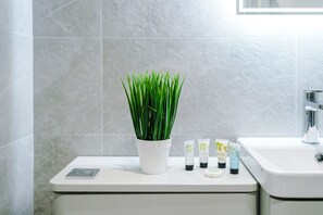 A bathroom with a white sink, a potted plant, and three skincare tubes on the counter.