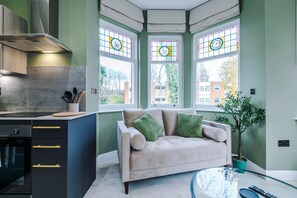 A modern kitchen with a built-in oven, a dining area with a glass table, and a sofa with green cushions.