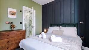 A bedroom with a bed, a dresser, a door, and a wall with a framed picture. - Hilltop Serviced Apartments - Stockport (Stockport)