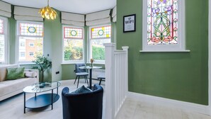 A room with a green wall, a white railing, a glass table, a sofa, and a chair. - Hilltop Serviced Apartments - Stockport (Stockport)
