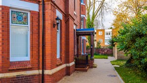 A red brick building with a white door and a small window. - Hilltop Serviced Apartments - Stockport (Stockport)