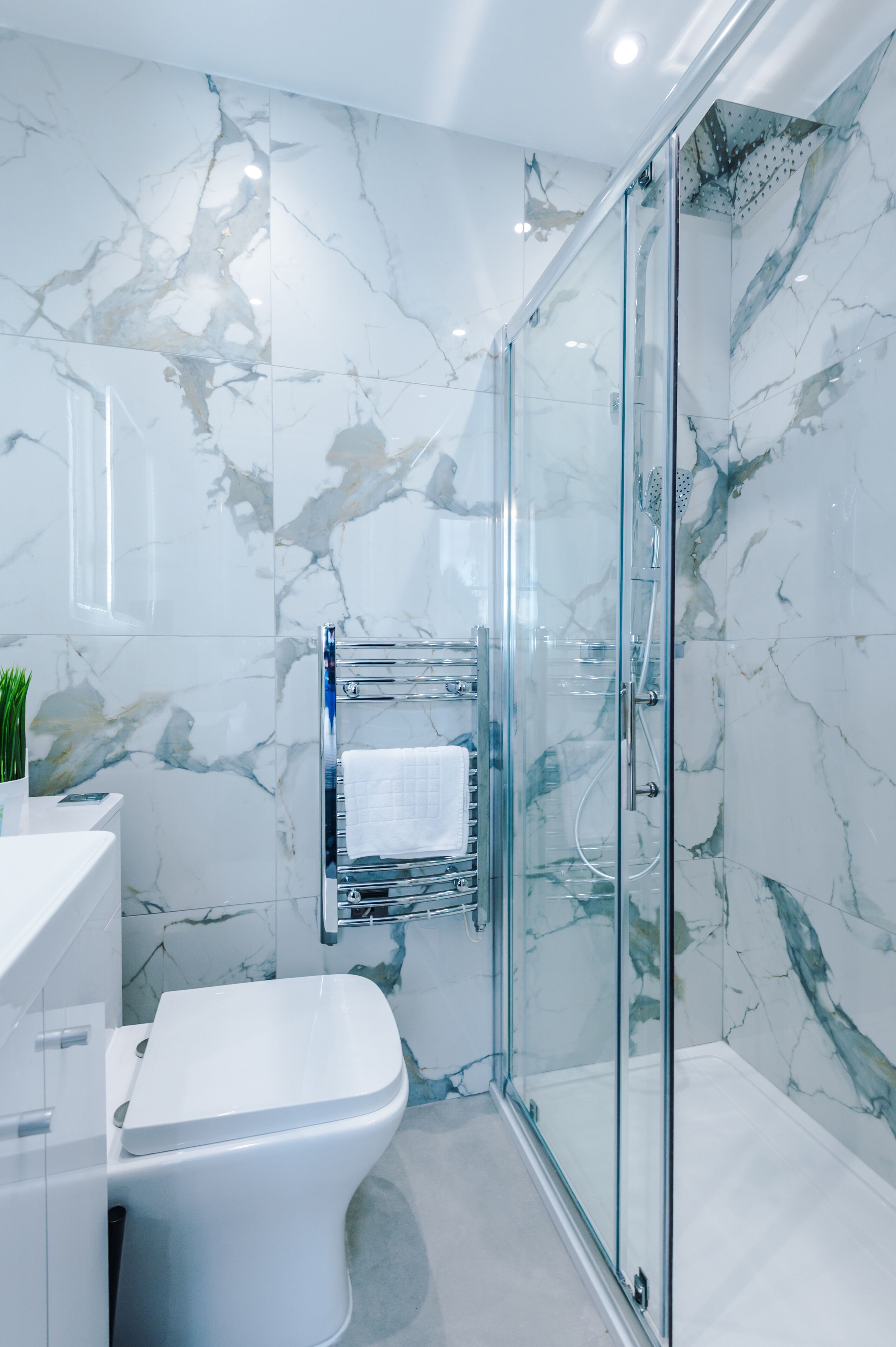 Un baño moderno con cabina de ducha de vidrio, inodoro blanco y salpicadero de mármol.