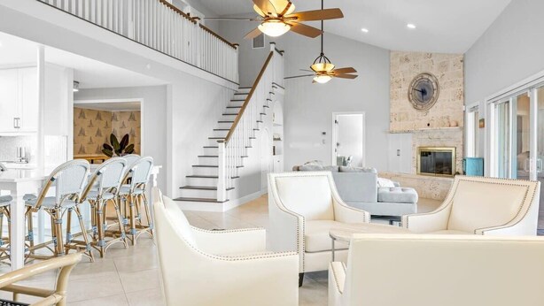 Amplia sala de estar con escalera, muebles blancos y ventiladores de techo.
