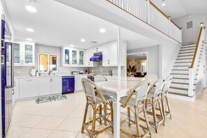 A modern kitchen with white cabinetry, a dining area with wicker chairs, and a staircase with a wooden railing.