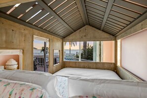 A room with two beds, wooden walls, a sloped ceiling, and a view of the sea.
