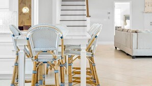Un interior moderno con comedor que incluye sillas de mimbre y una mesa blanca, una escalera y un ventilador de techo.