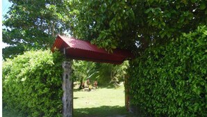Un espace extérieur abrité, doté d’un pilier en pierre, entouré d’une végétation luxuriante et bordé d’un sentier herbeux.