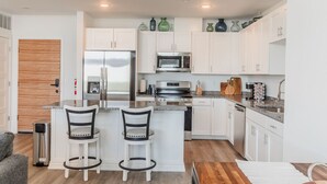 Una cocina moderna con armarios blancos, electrodomésticos de acero inoxidable y una barra con dos taburetes.