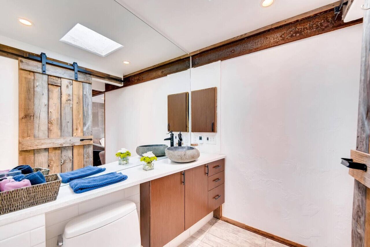 A modern bathroom with a wooden sliding door, a white vanity with a large mirror, and a stone sink.