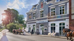A historic building with a sign for 'Fettehenné Catering' and a horse-drawn carriage on the street.