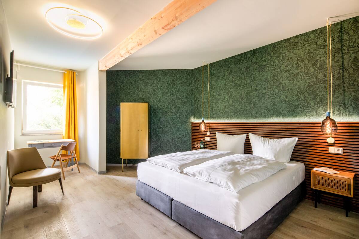 A modern bedroom with a large bed, wooden headboard, and a desk with a chair.