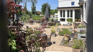 An outdoor patio area with tables and chairs, surrounded by potted plants and trees.