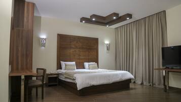 A modern hotel room with a wooden headboard, a bed with white bedding, a desk with a chair, and a television.