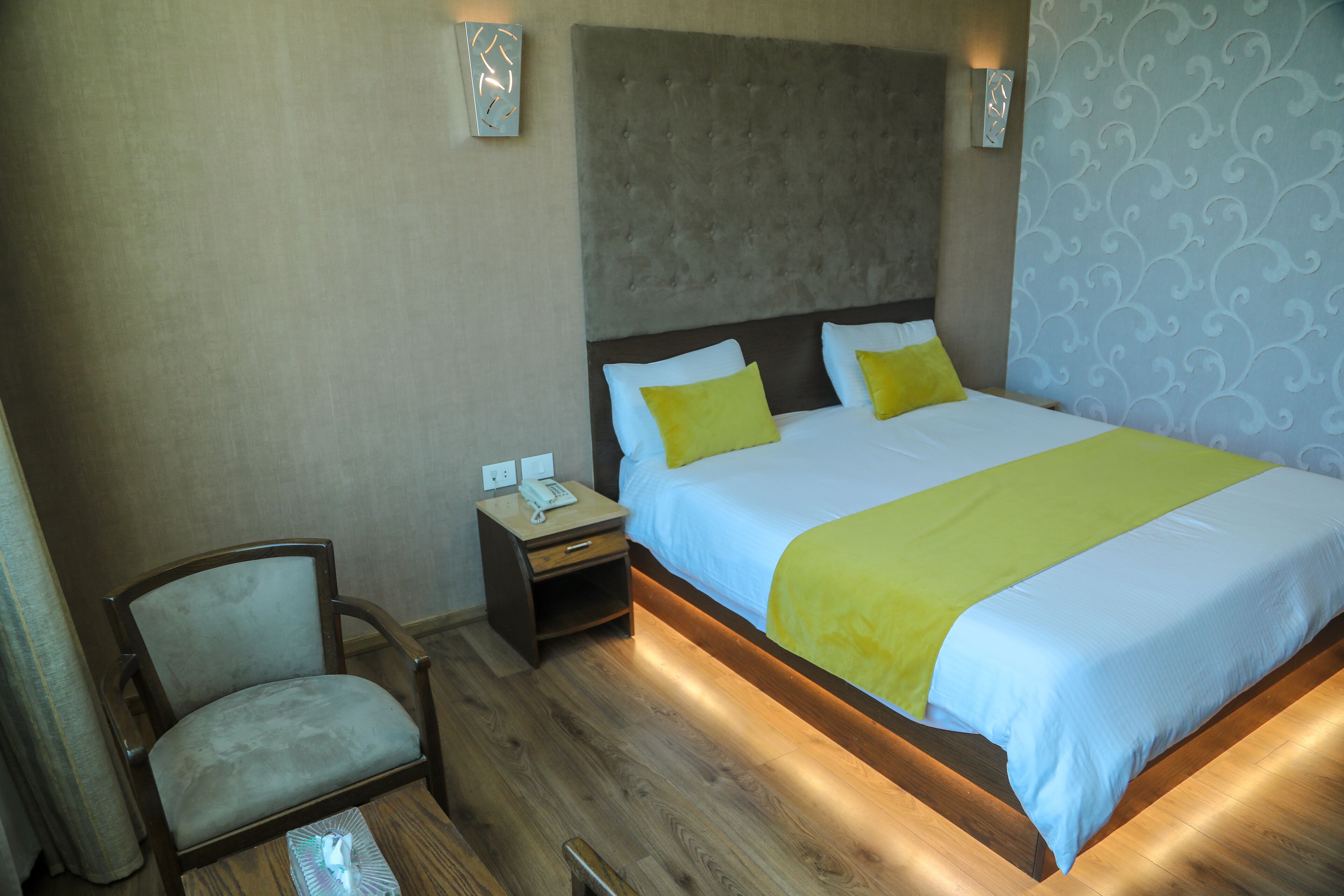 Una camera d'albergo con un letto, un comodino, una sedia e una parete con decorazioni.