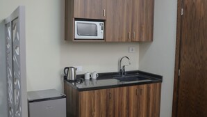 A compact kitchen with wooden cabinets, a built-in microwave, a small refrigerator, and a sink. - Eden Hotel (Jdeideh)