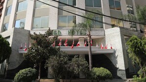 A tall, modern hotel with a curved facade, multiple windows, and a series of flags at the entrance. - Eden Hotel (Jdeideh)