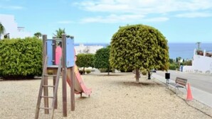 A playground with a slide and climbing structure, surrounded by gravel and trees. - Heart of Mojacar Playa with Beautiful " see view " and Sunshine (Ventanicas-el Cantal)