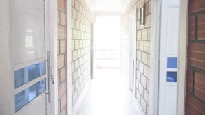 A narrow hallway with brick walls and white doors, leading to a bright area at the end.