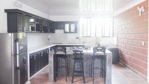 A modern kitchen with dark cabinets, a stainless steel refrigerator, a gas stove, and a central island with bar stools.