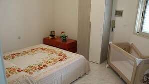 A bedroom with a bed, a dresser, a crib, and a window. - Trilocale Glicine piano terra Baia Verde (Gallipoli)