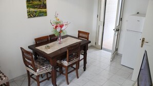A dining area with a wooden table, four chairs, a vase with flowers, and a painting on the wall. - Trilocale Glicine piano terra Baia Verde (Gallipoli)