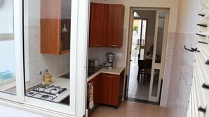 A compact kitchen with wooden cabinets, a gas stove, and a coffee maker. - Trilocale Glicine piano terra Baia Verde (Gallipoli)