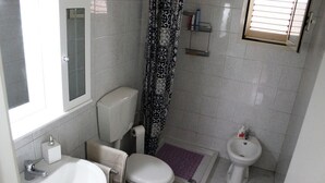 A compact bathroom with a toilet, bidet, sink, and a window with blinds. - Trilocale Glicine piano terra Baia Verde (Gallipoli)