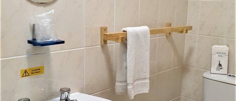 A bathroom with a sink, mirror, towel rack, toilet, and a caution sign for hot water.