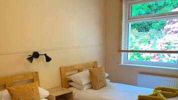 A hotel room with two single beds, a nightstand, a lamp, and a window with a view of greenery.