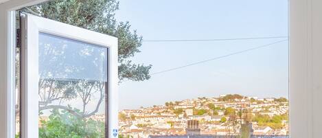 Un comedor con una mesa dispuesta para cuatro personas, vistas a un pueblo en la ladera a través de un ventanal, y cielo despejado.