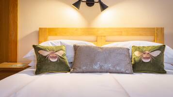 A neatly made bed with a wooden headboard, two decorative pillows with a bee design, and a wall-mounted light fixture.