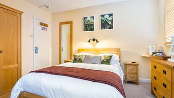 A bedroom with a bed, wooden dresser, nightstand, and wall art.