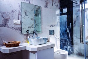 Un baño moderno con salpicadero de mármol, un lavamanos grande tipo pedestal, un inodoro blanco y una zona de ducha con cerramiento de vidrio.