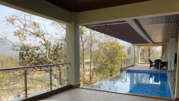 A pool area with a view of trees and a balcony with a railing.
