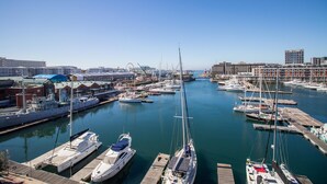 A marina with multiple boats docked, a clear sky, and buildings in the background.