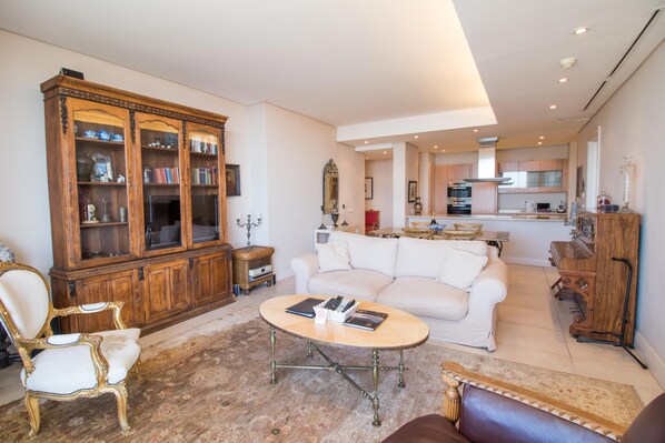 A living room with a white sofa, a coffee table, a wooden cabinet, and a dining area in the background.