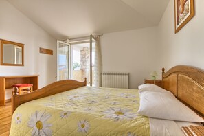 Een slaapkamer met een houten bed, een rode stoel, een nachtkastje van hout met een lamp, en uitzicht op het omliggende landschap.